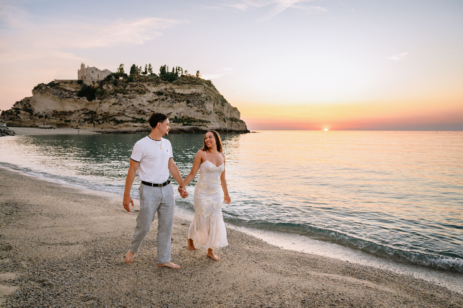 Couple holding hands while walking along the water during an engagement shoot in Tropea