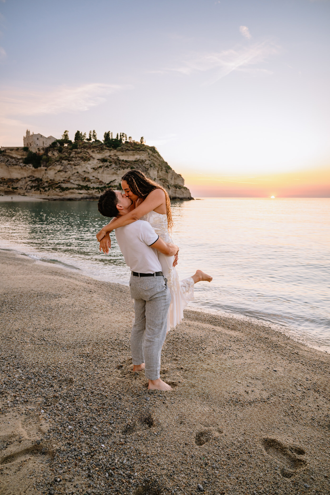 Wide angle shot of a couple standing together on the beach in Tropea at sunset